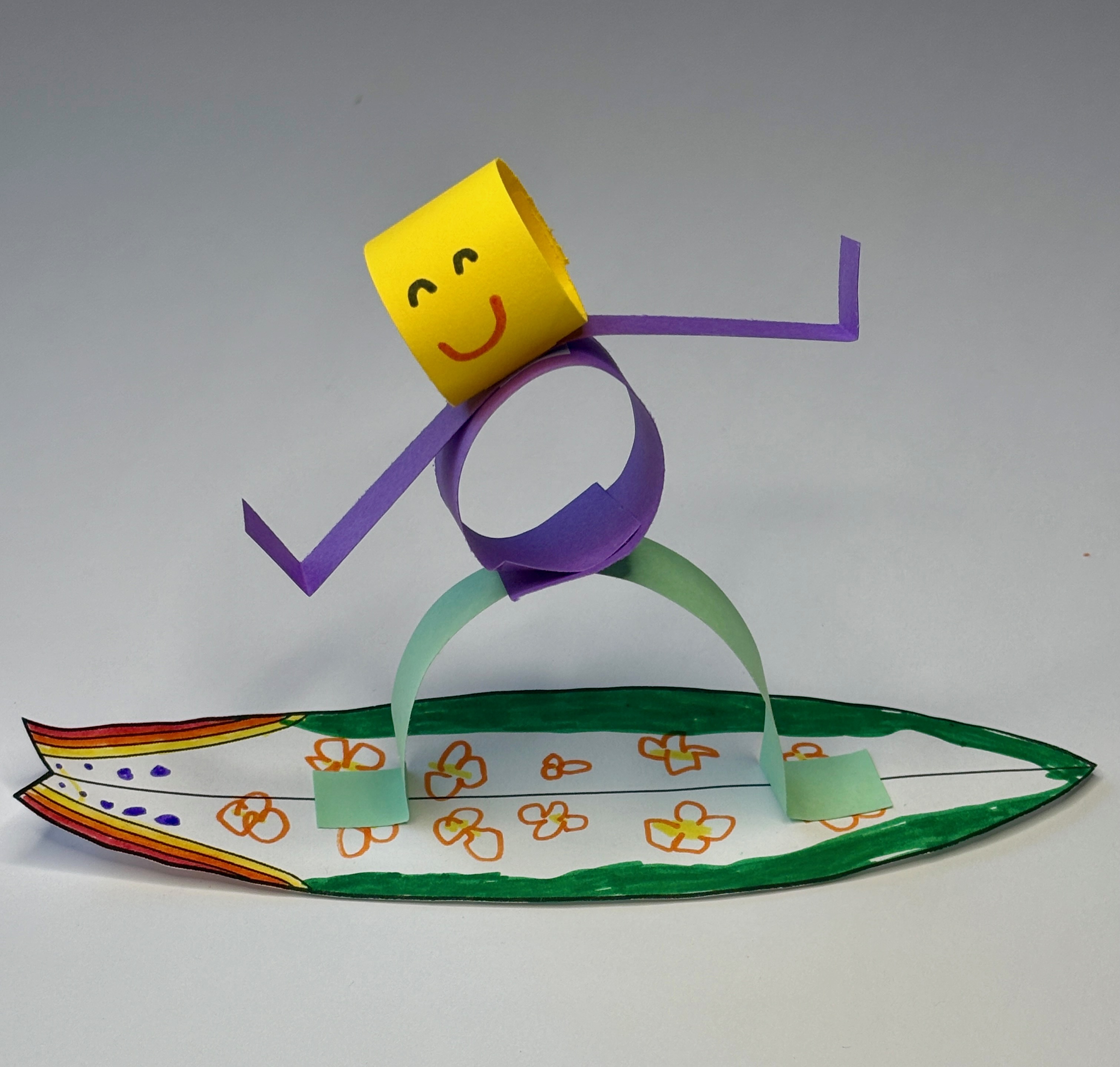 Violet's paper surfer craft: a smiling paper figure riding a hand-colored surfboard